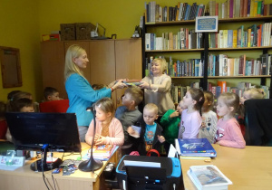 Pani Małgorzata Hofamnn przekazuje pani Agnieszce Piekarskiej książki. Dzieci stoją wokół pań.